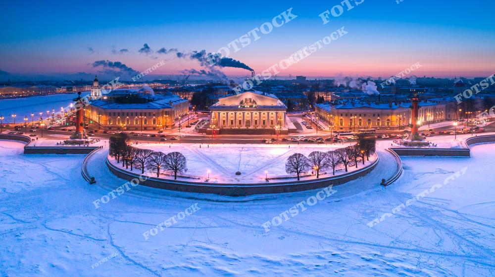 На фотографии изображена Стрелка Васильевского острова, окружённая льдами Невы в зимнее утро. Здание Биржи, освещённое мягким светом, занимает центральное место, а Ростральные колонны создают симметрию на обеих сторонах. Небо окрашено в нежные розовые и голубые тона, подчёркивая красоту зимнего Санкт-Петербурга.